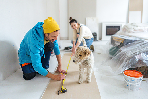 Ein Paar steht vor seinem Haus und hält gemeinsam ein Solarpanel, beide lächeln.